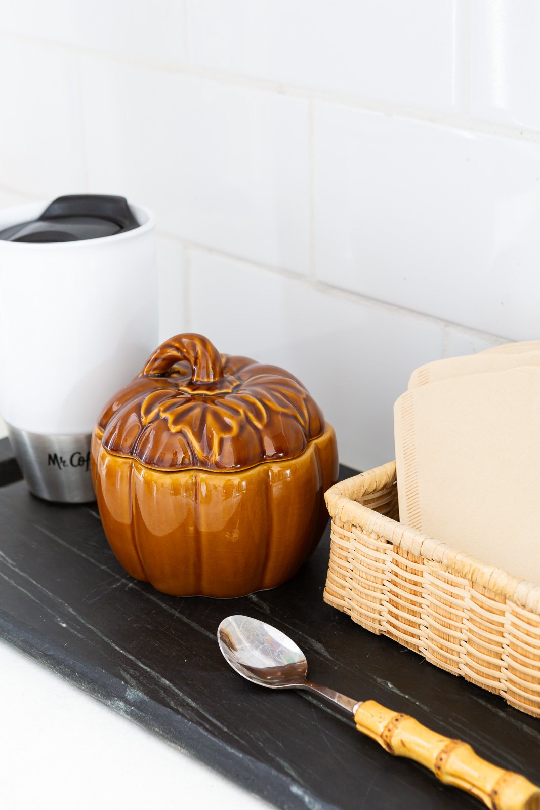 brown ceramic pumpkin bowl with lid to hold sugar for the fall season placed on a kitchen counter coffee station.