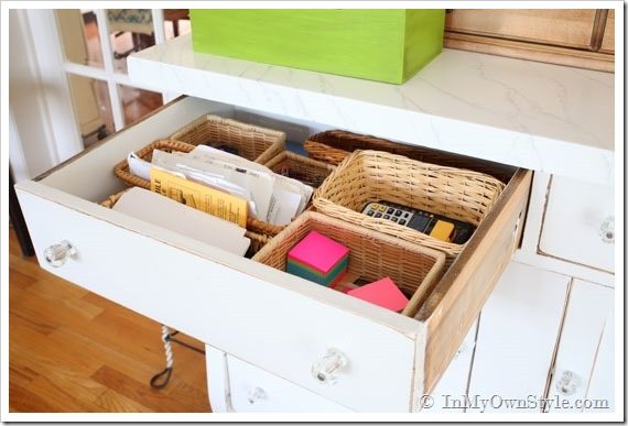 Desk drawer with contents organized in small low sided baskets.