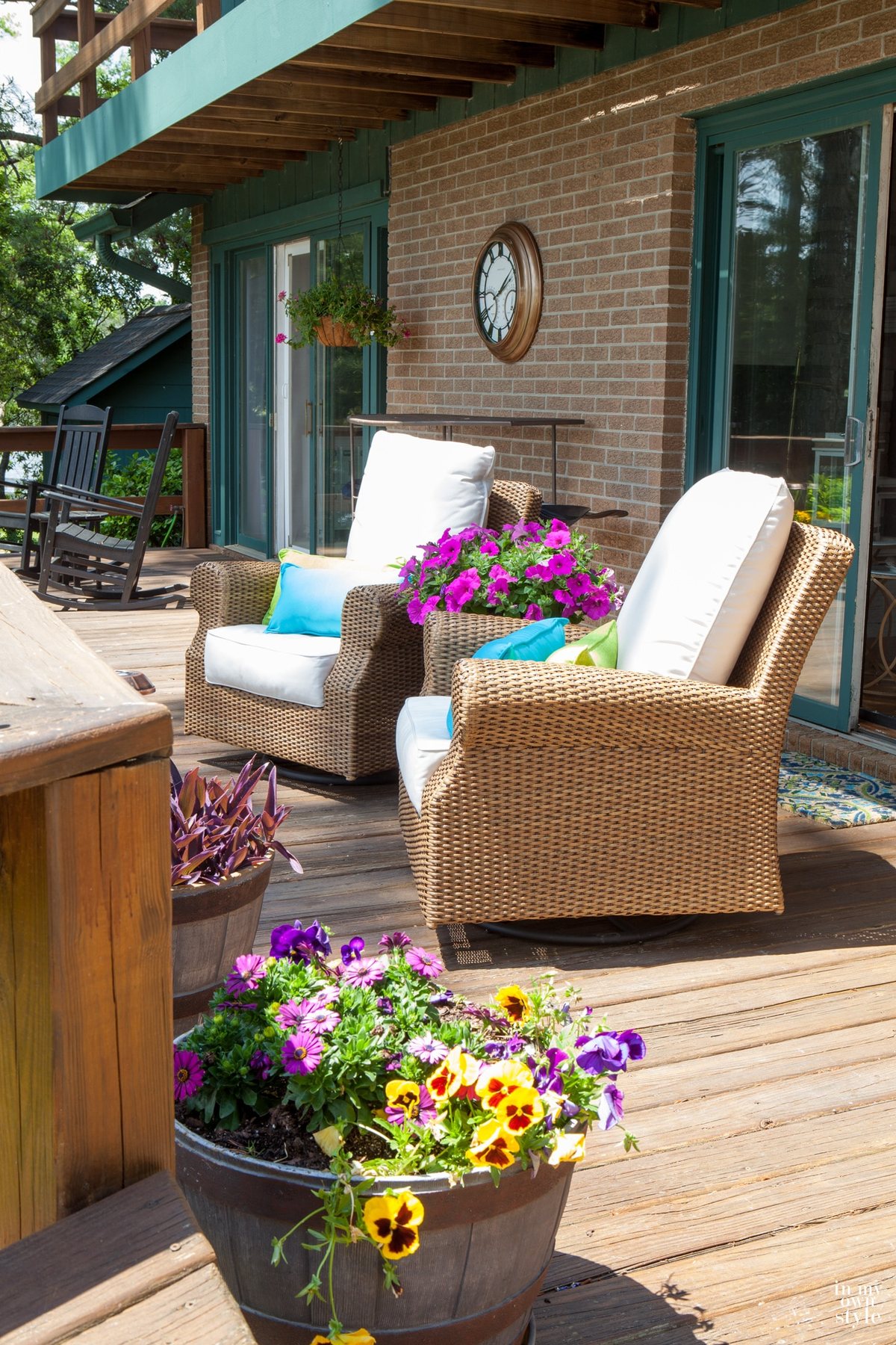 Two rattan chairs and planters with purple and yellow pansies on deck.