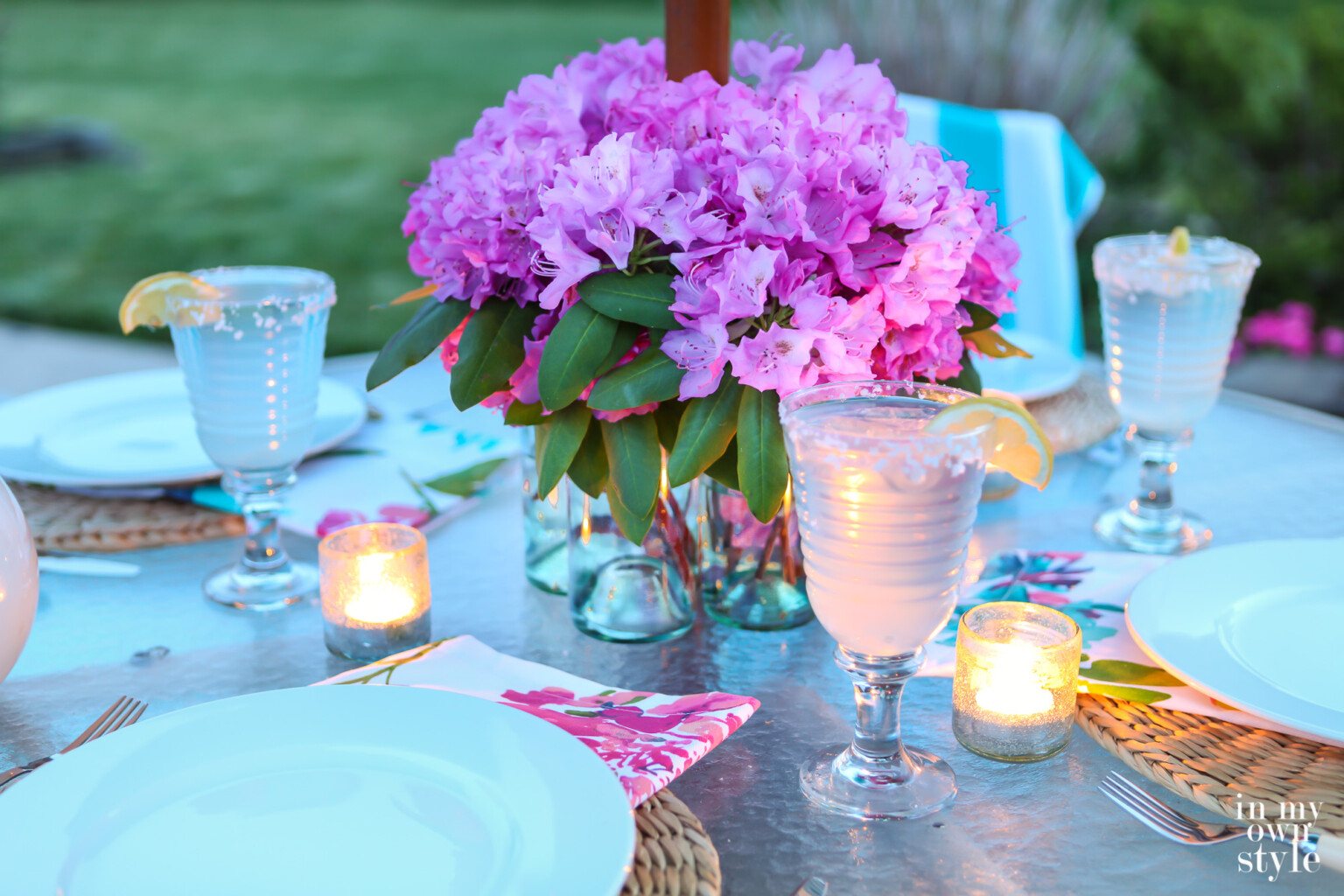Umbrella patio table centerpiece made using glass bottles. Table set and candles are lit on table.