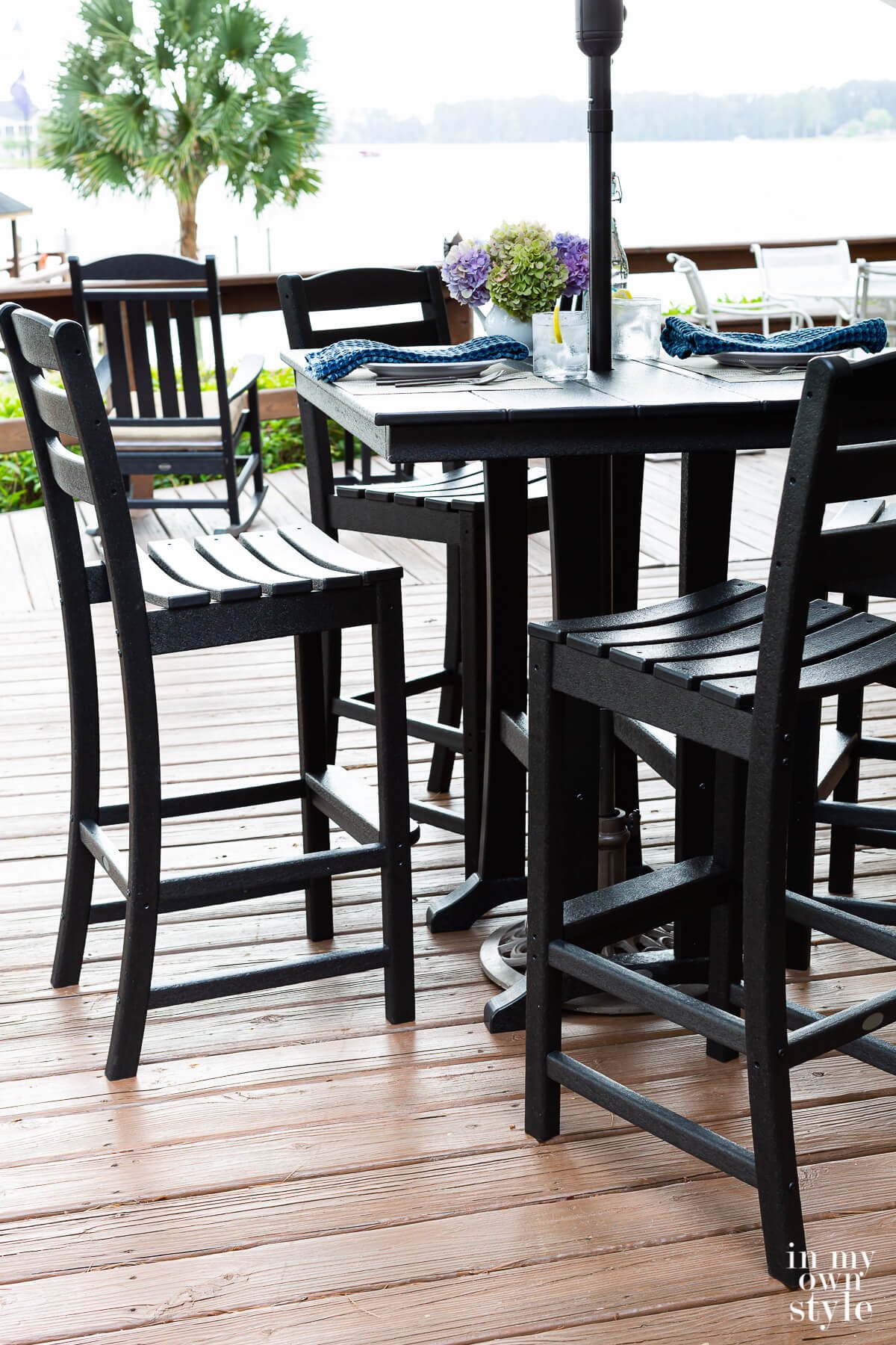 A set of black POLYWOOD outdoor dining furniture on a deck over looking a lake.