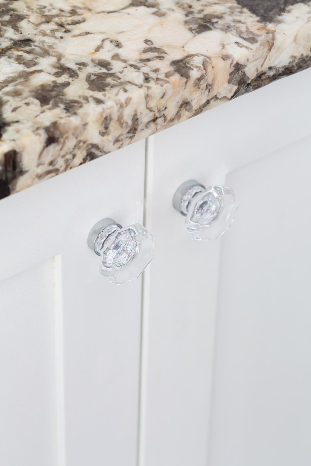 glass and polished chrome cabinet knobs on white bathroom cabinets.