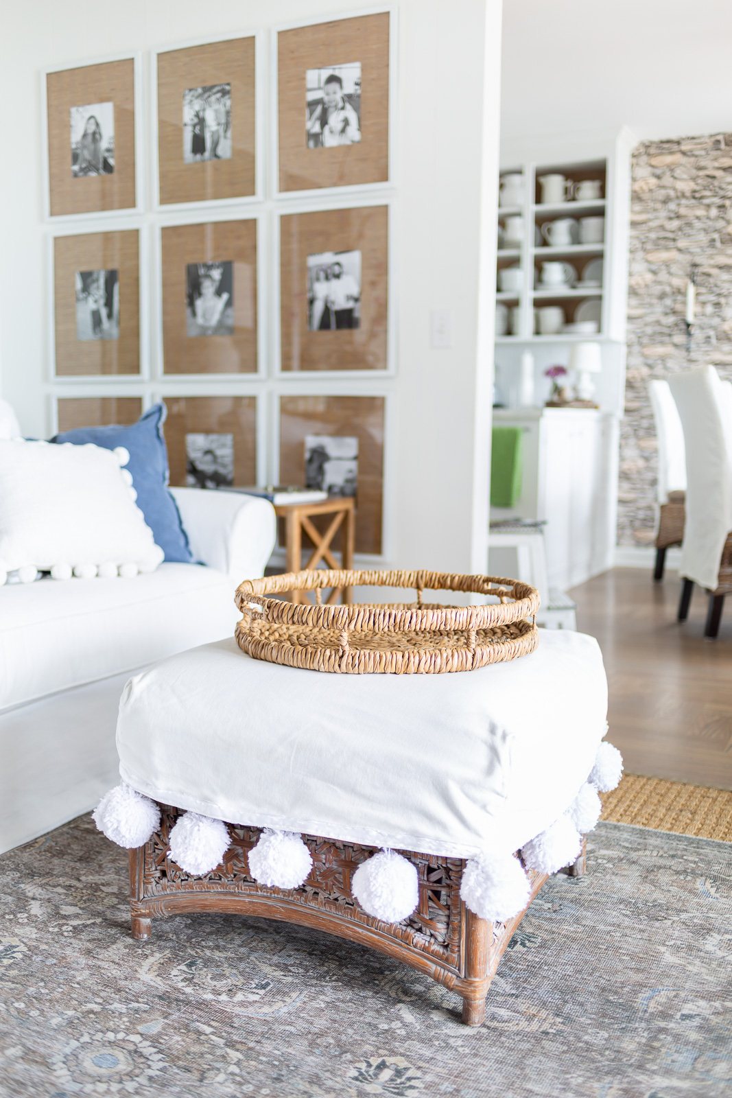 Round rattan tray on white slipcovered ottoman in a living room.