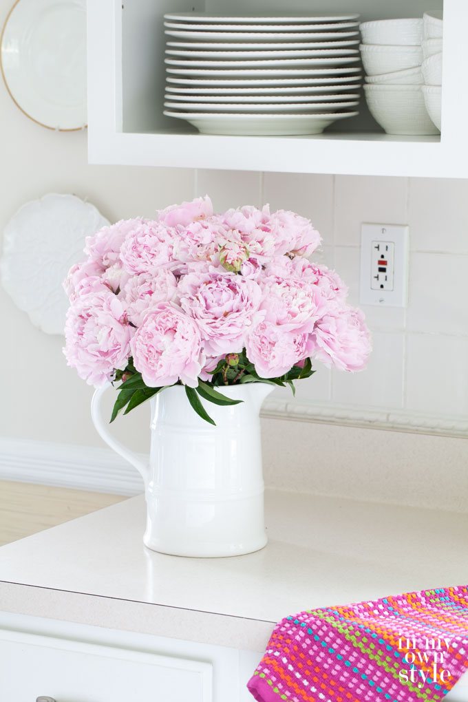 Pretty peonies on kitchen counter under cabinets with no doors..