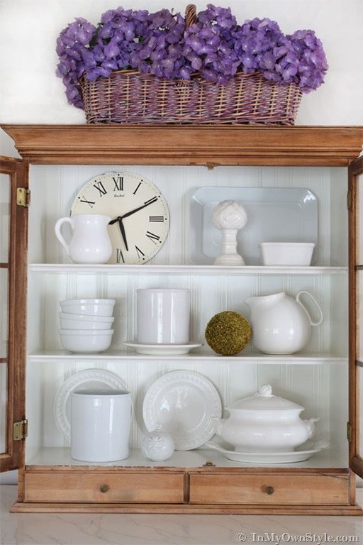 Open kitchen cabinet styling idea using white dish ware, pitchers and decorative accessories.