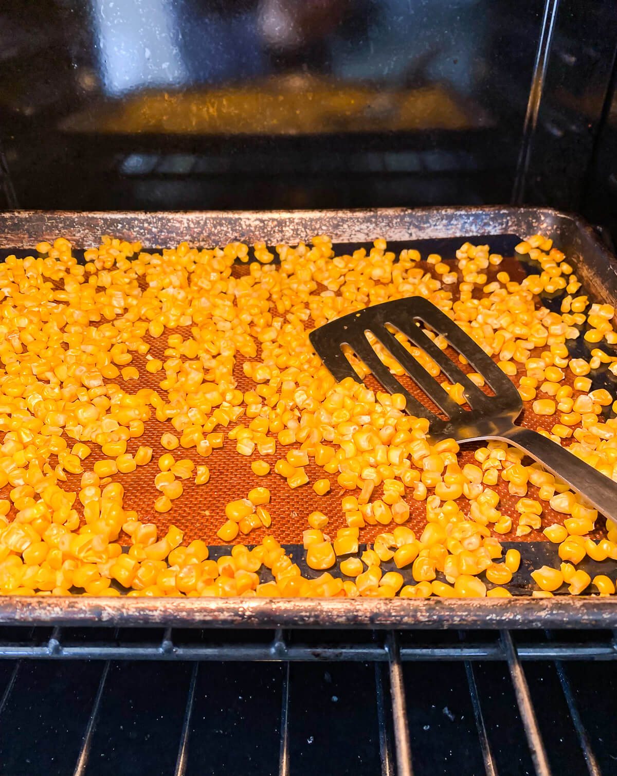 Frozen corn kernels on a baking tray in an over getting roasted.