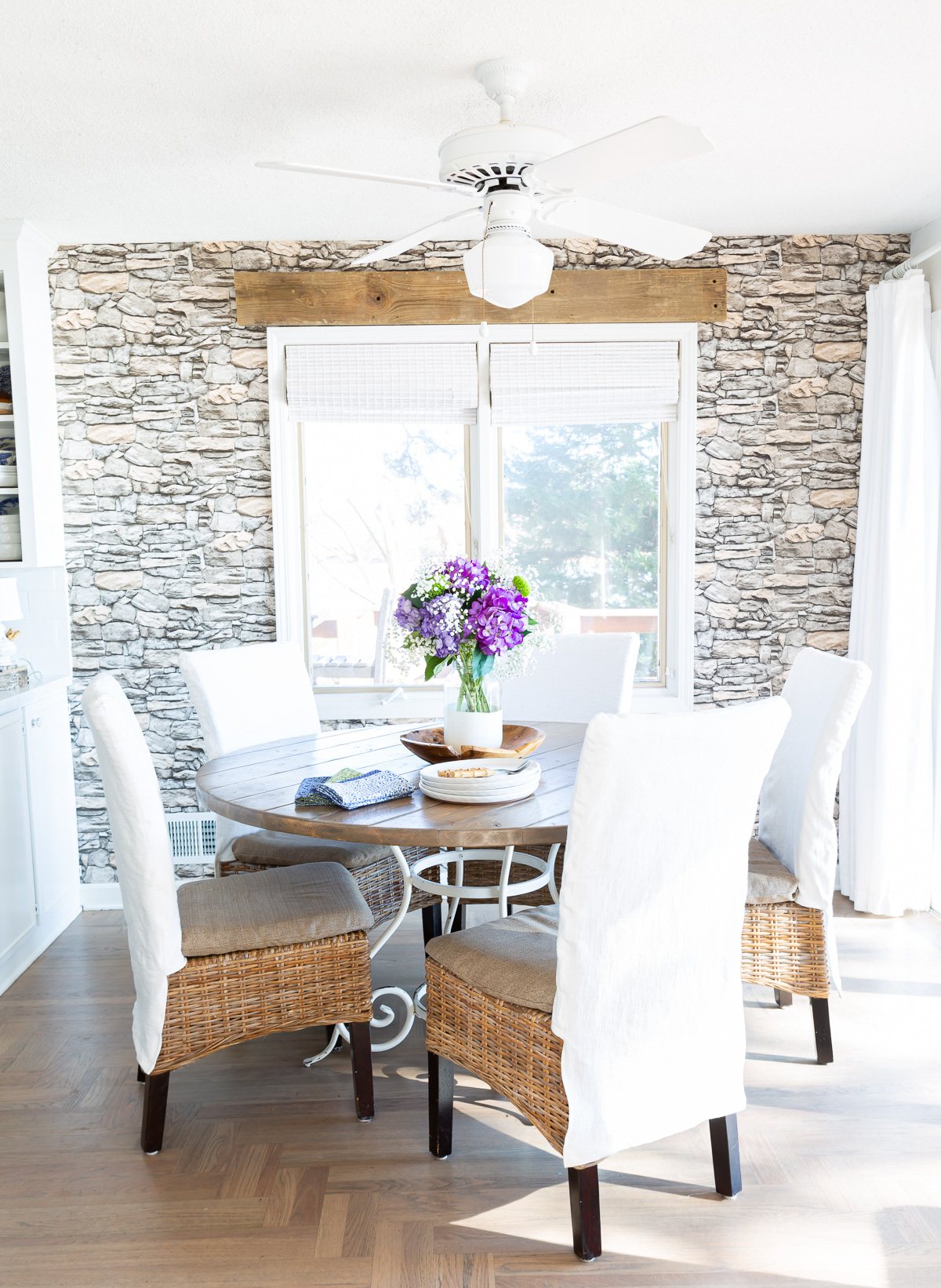 Kitchen table with 5 dining chairs around it each with a white slipcover.