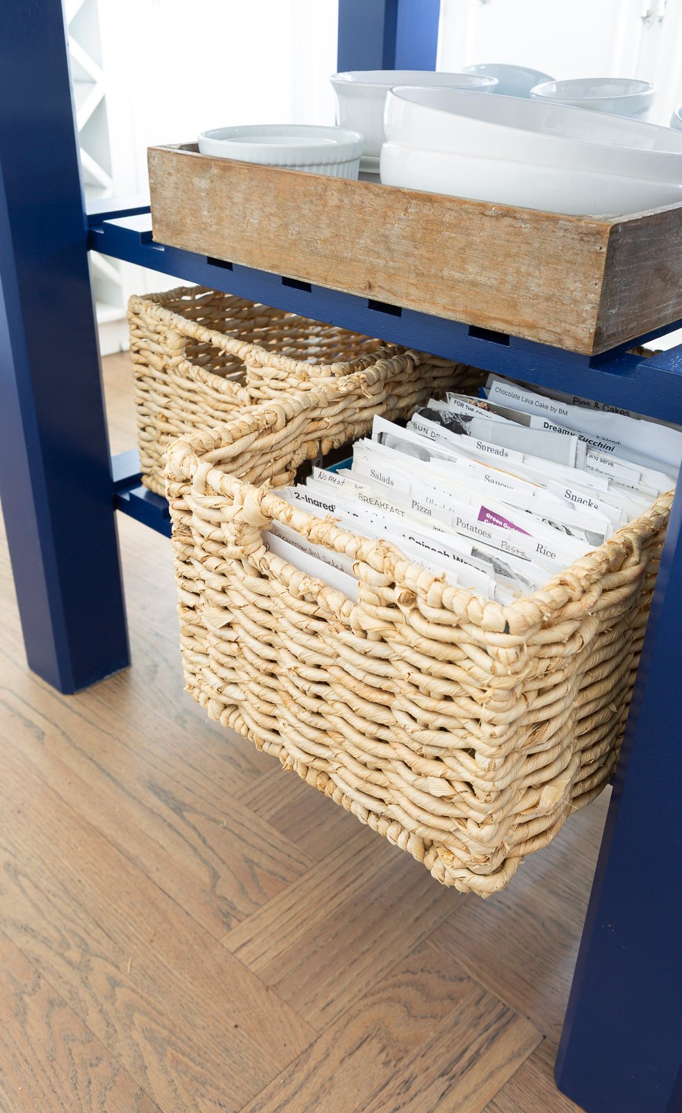 View of bottom shelf on small kitchen work table island with two baskets - one pulled out to shop it acts as a recipe box.
