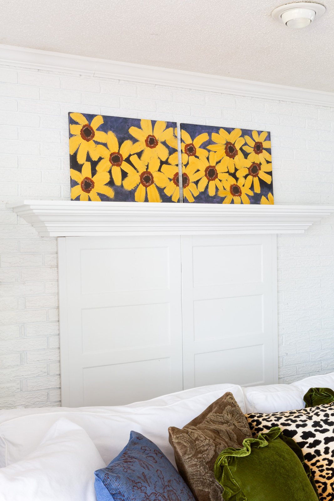 Painted fall flowers on a canvas leaning on a white fireplace mantel.