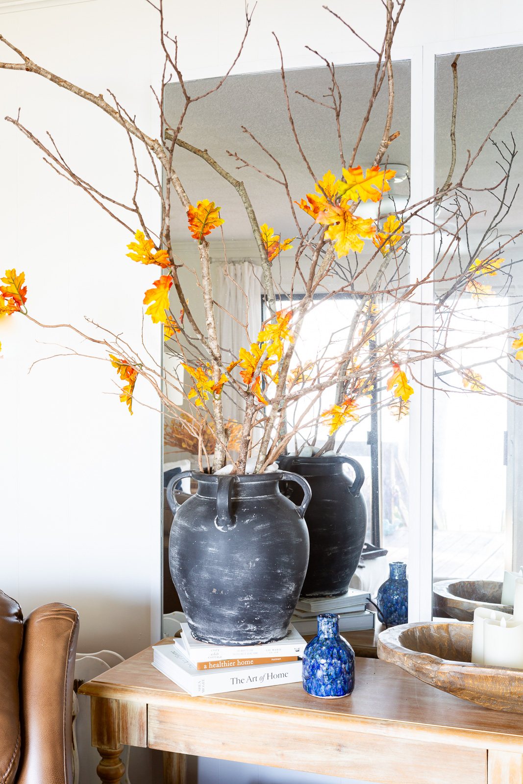 Faux fall leaves on bare tree branches in a large black vase on a console table.