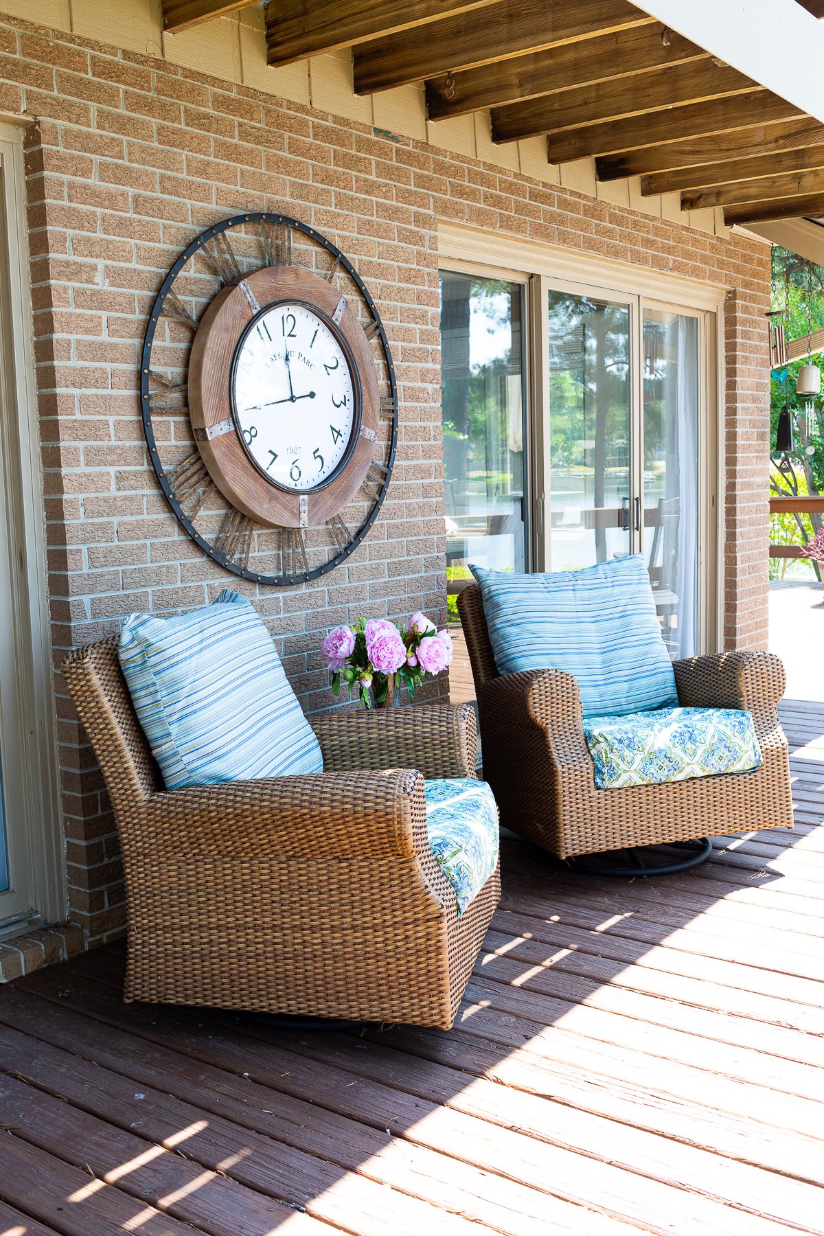 outdoor wall clock hanging on brick wall on a deck.