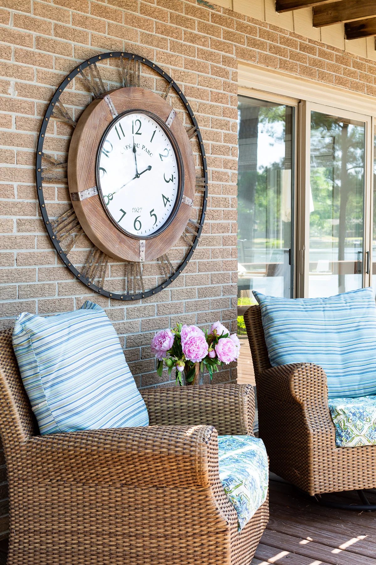Oversized outdoor wall clock hanging on an exterior brick wall surrounded by outdoor furniture.