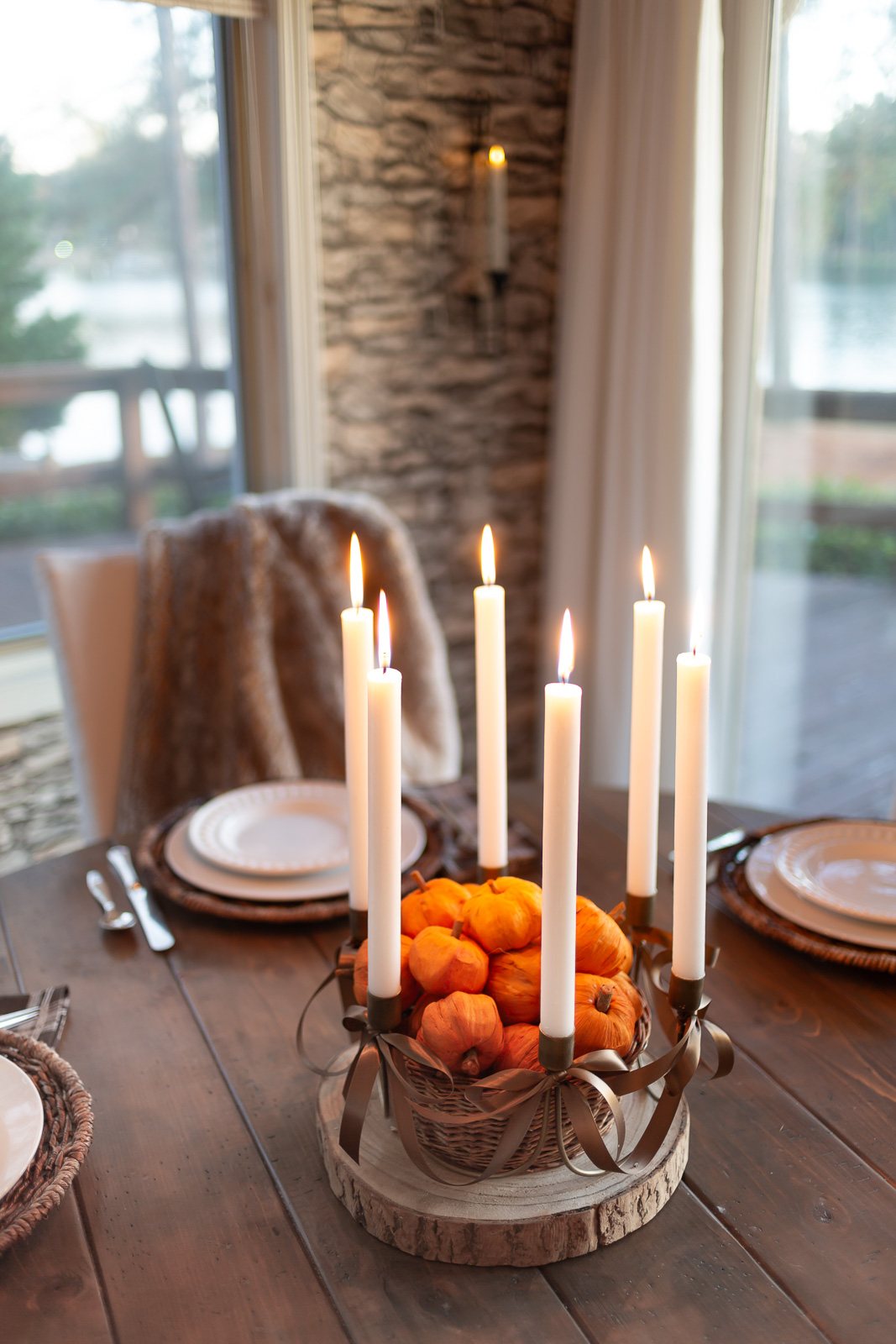 Antique Brass 6 taper candle centerpiece with brown ribbon bows added on wood slice on table. Center has basket filled with tiny paper pumpkins.