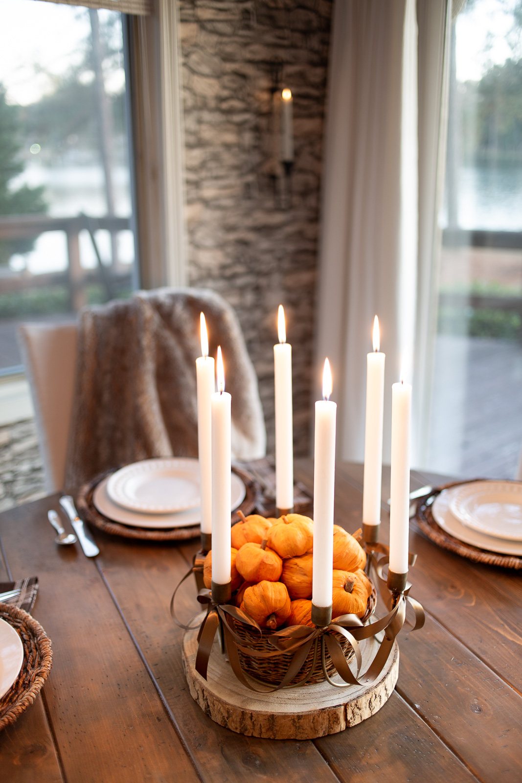 Antique Brass 6 taper candle centerpiece with brown ribbon bows added on wood slice on table. Center has basket filled with tiny paper pumpkins.