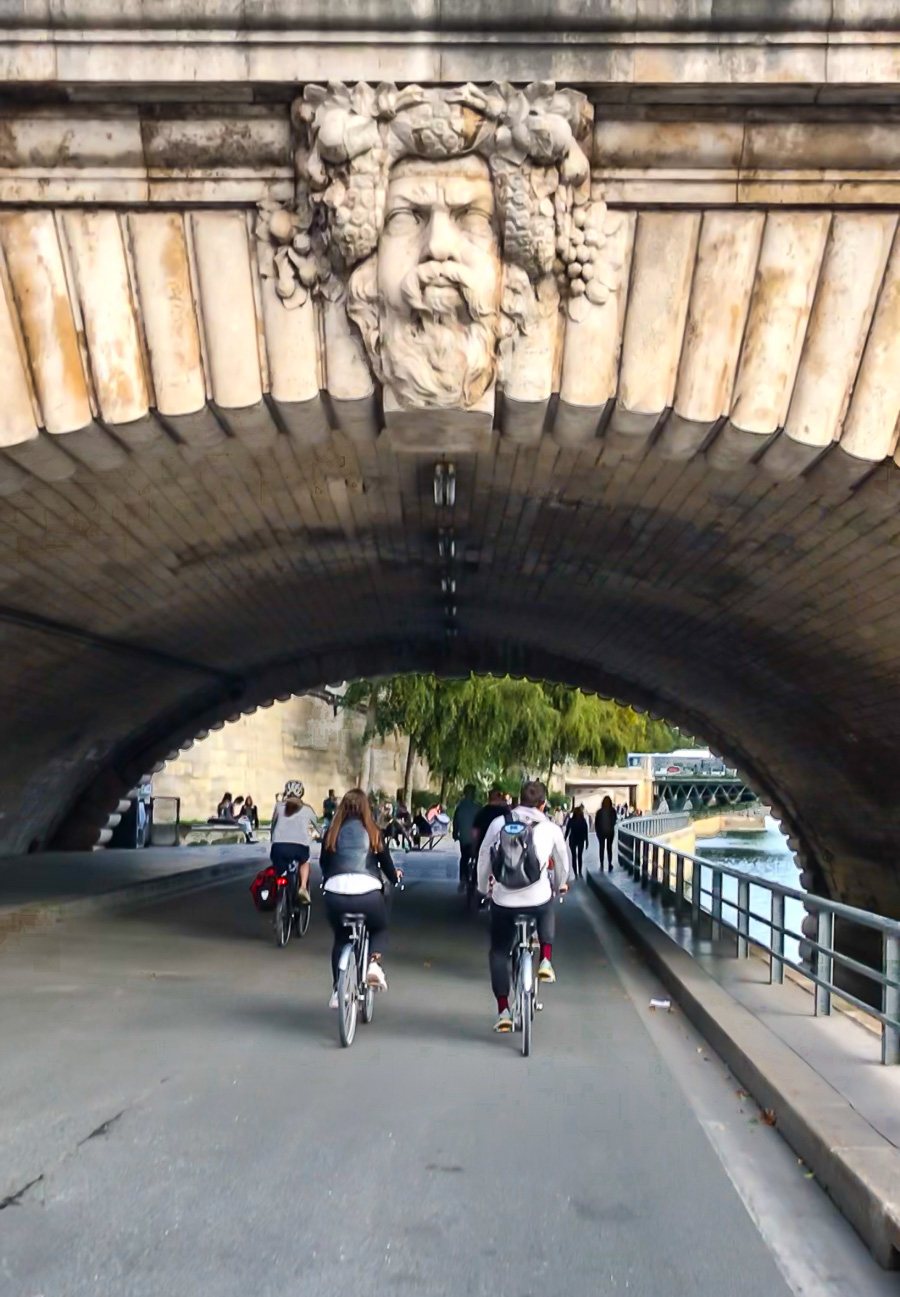 Riding in a bike tour group in Paris under a bridge along the Seine with Bike About Tours Paris.
