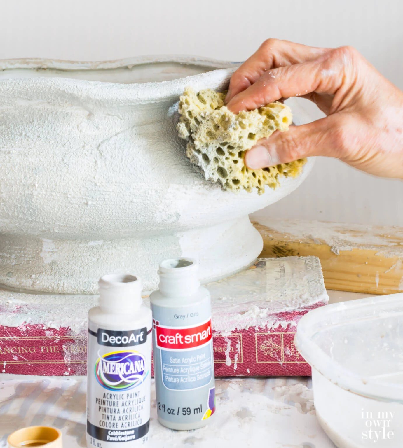 Using a sea sponge to apply paint over texture layer of stucco patch on large bowl planter.