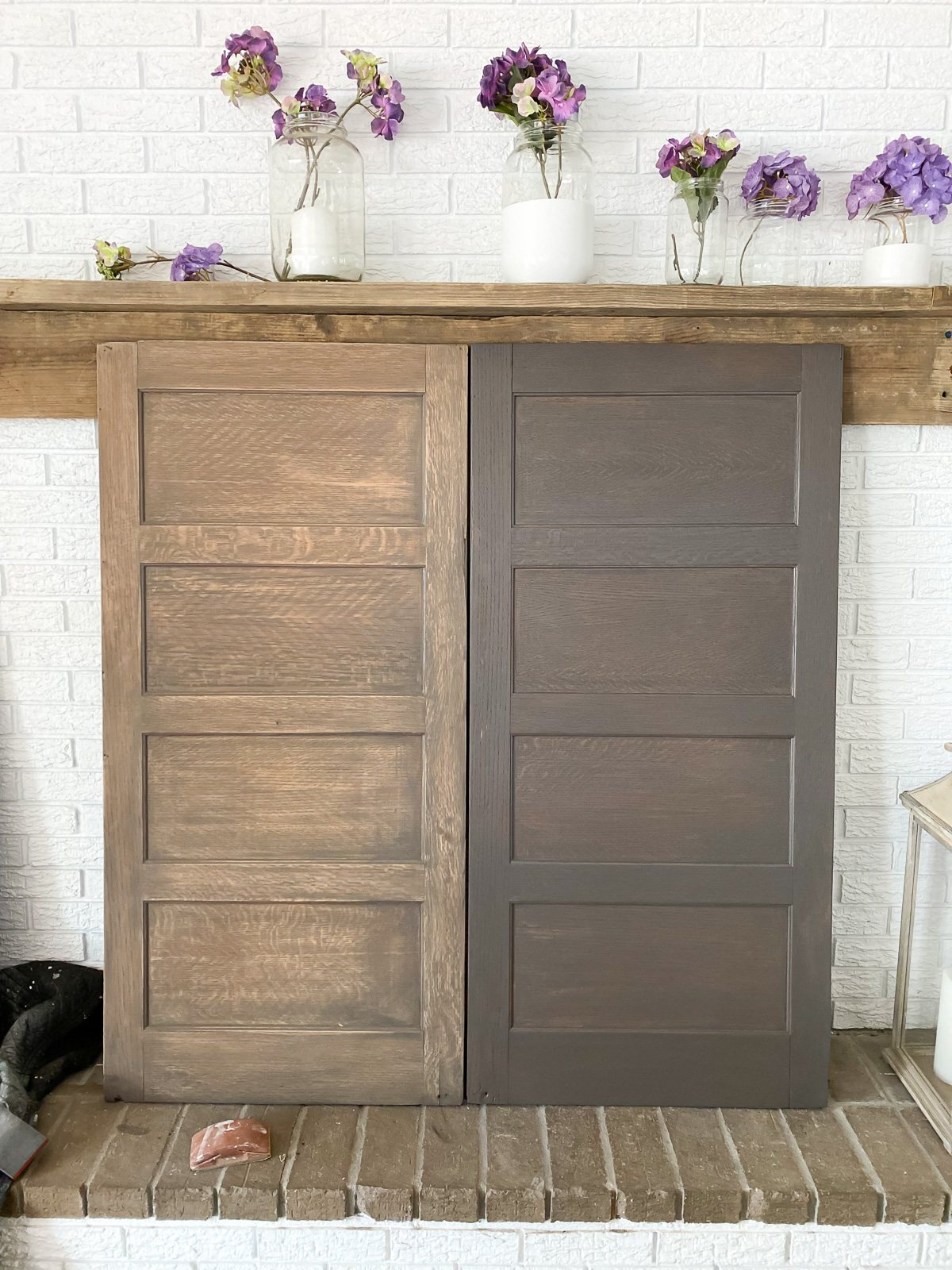 two wood panels leaning against a fireplace wall. One is sanded to lighten in, the other is stained in a driftwood shade.