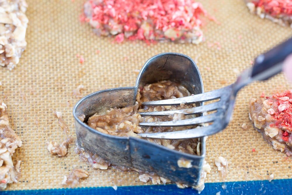 Banana oatmeal cookie batter being pressed into a heart cookie cutter using a fork.