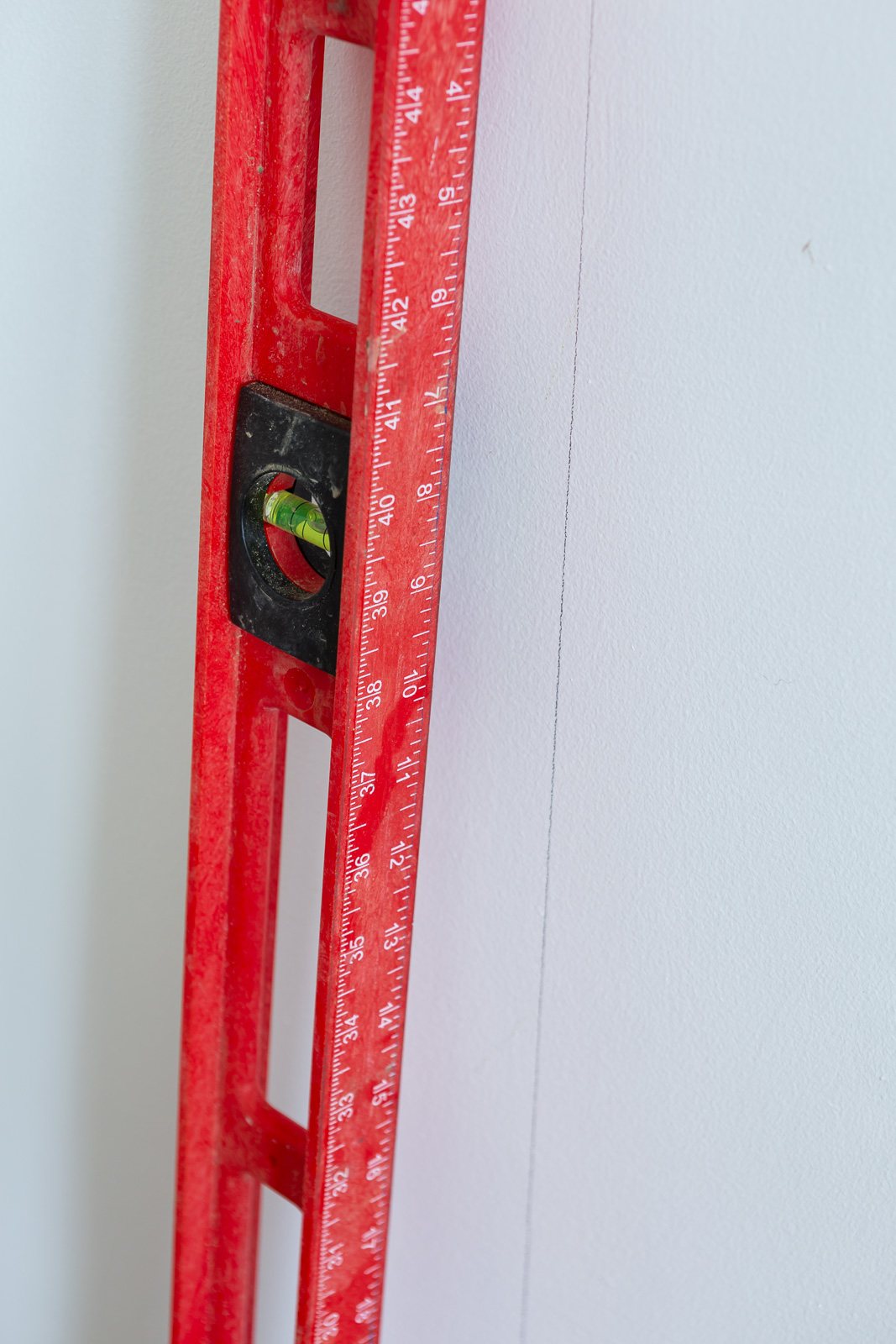 red bubble level being use to make a level vertical line to place first panel of wallpaper on a wall.