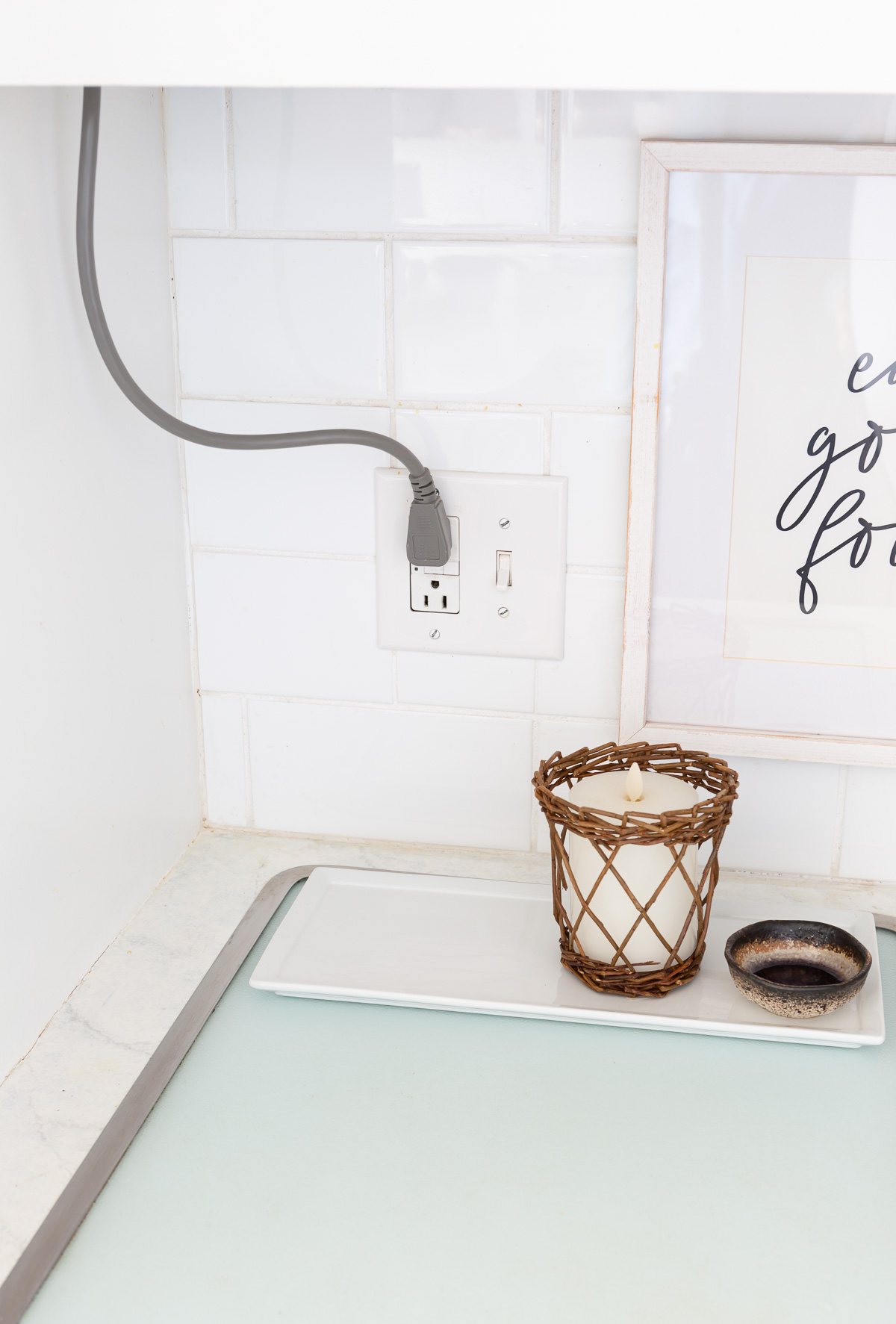 A corner on a kitchen counter and backsplash where an electrical cords comes down from the upper cabinets.