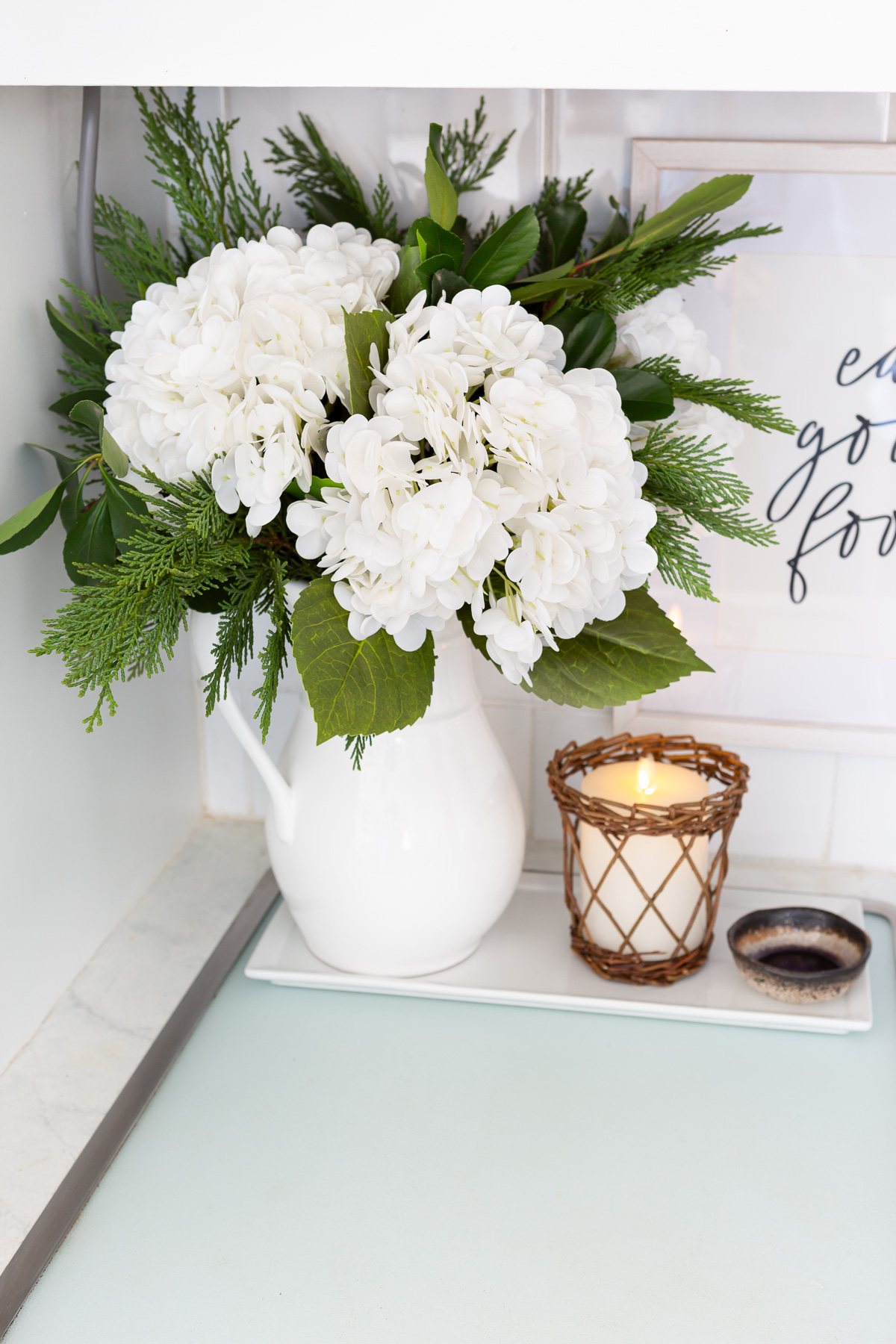 Winter white large head hydrangeas and greenery mixed in a white pitcher becomes cheery winter decor.
