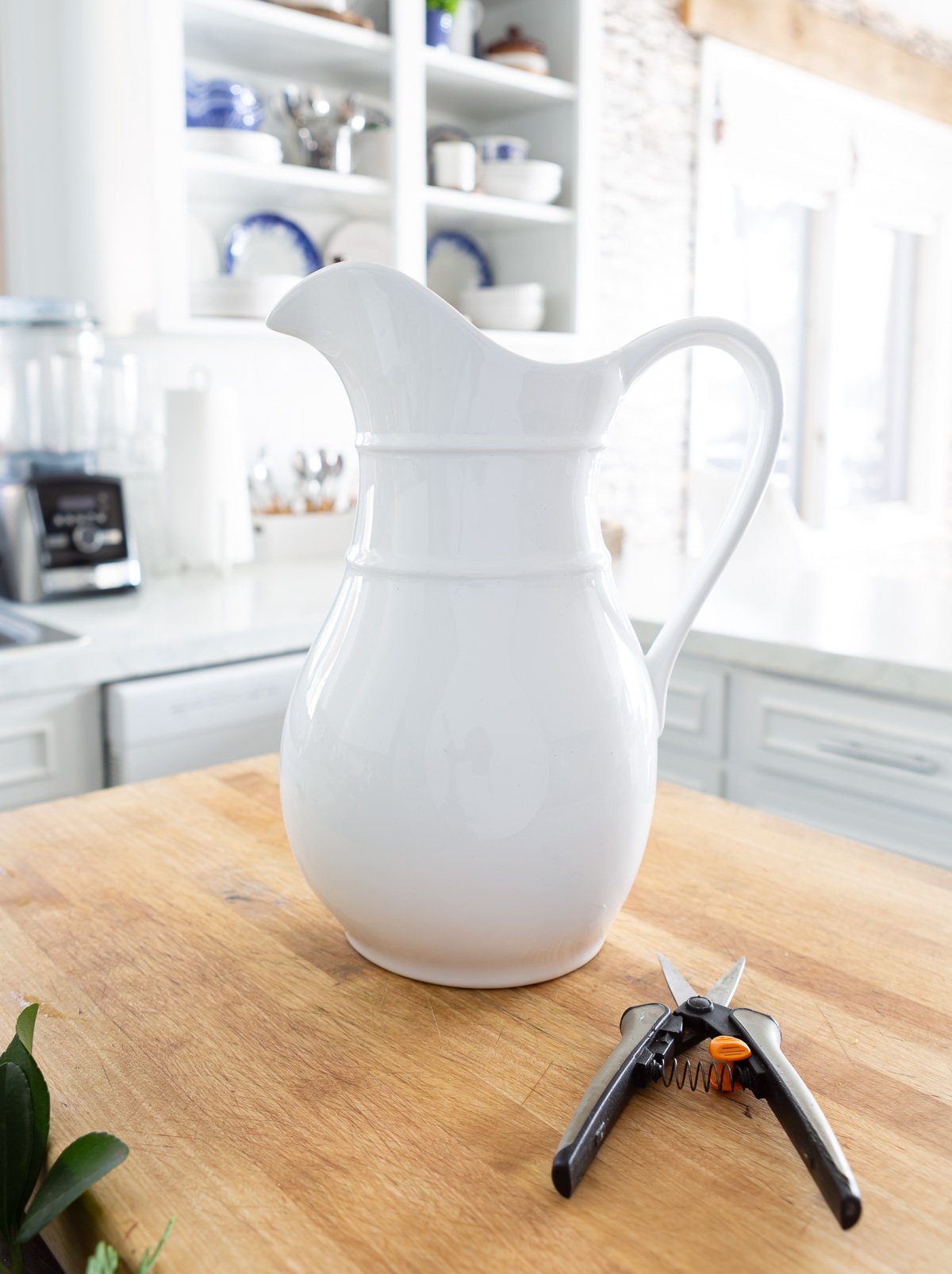 A tall white ceramic pitcher and gardening snips on a kitchen counter.