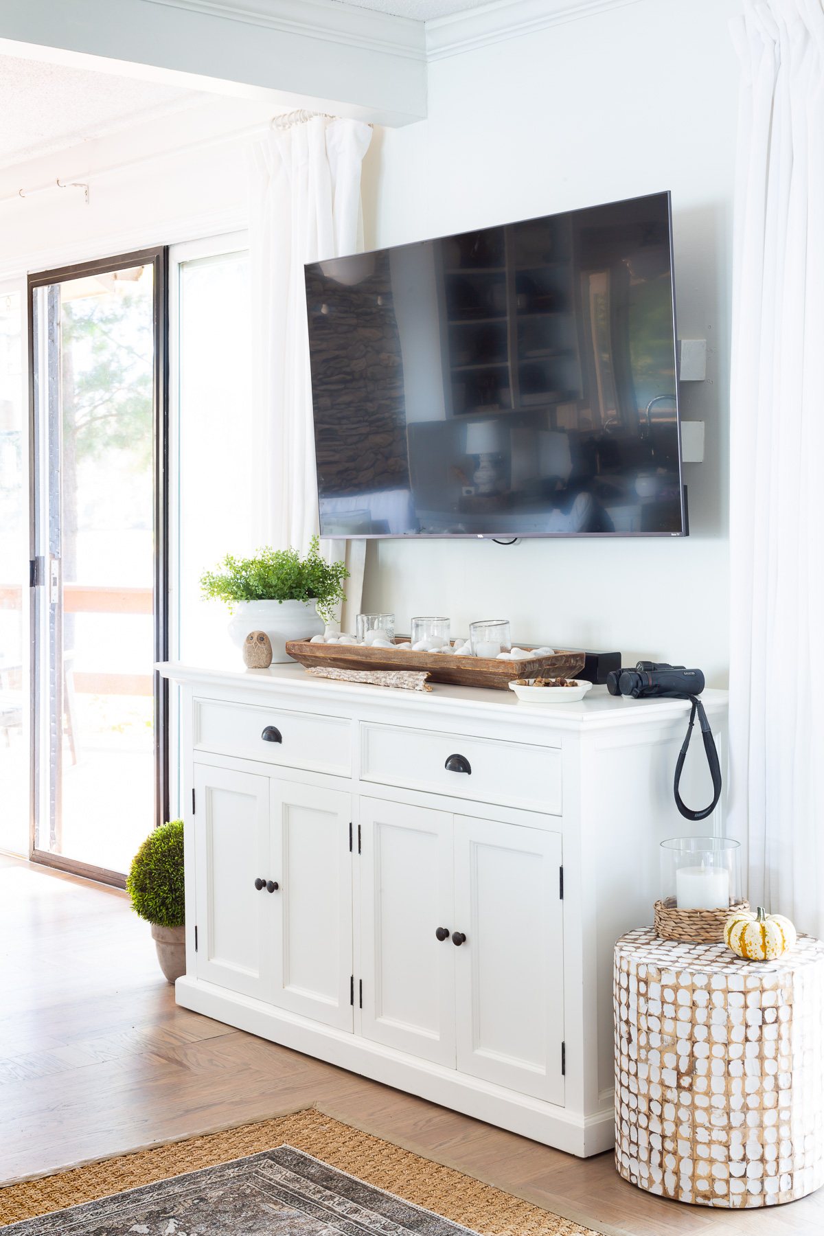 Black flat screen TV mounted on wall with white sideboard underneath.