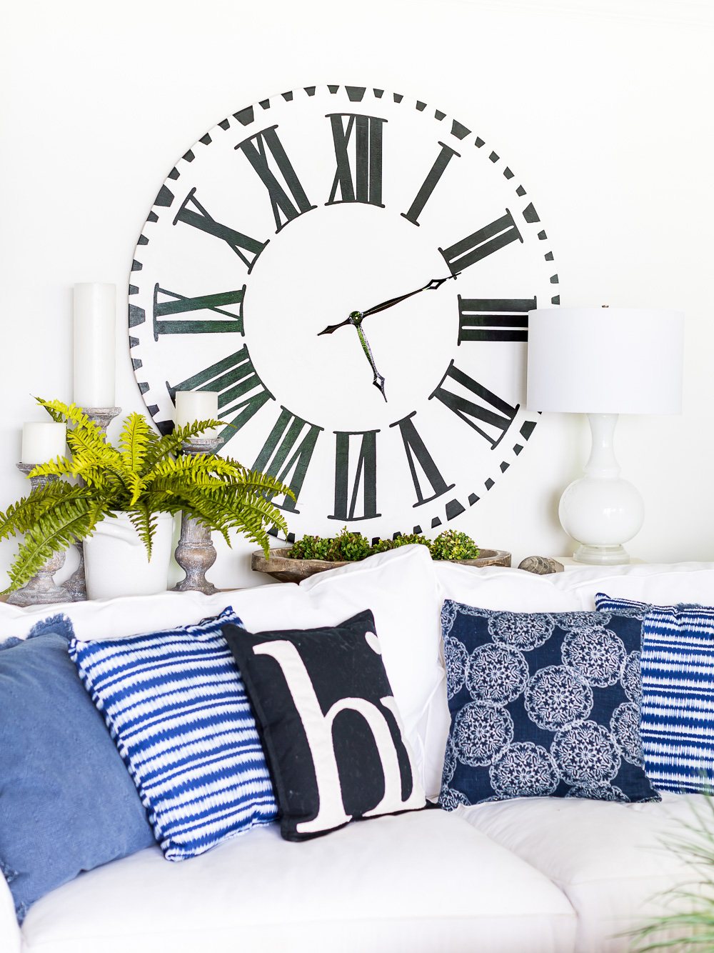 White faced Roman numeral oversized clock on wall in blue and white decorated living room