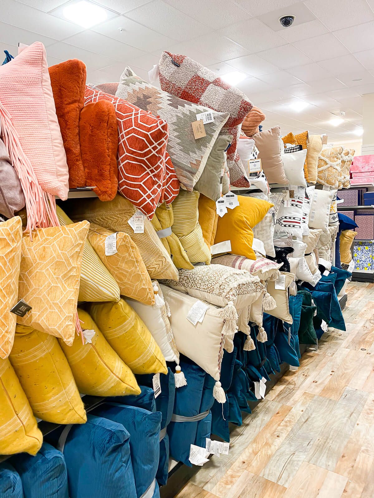 Toss pillows on display in the aisle at Home Goods in the colors yellow, blue and orange.