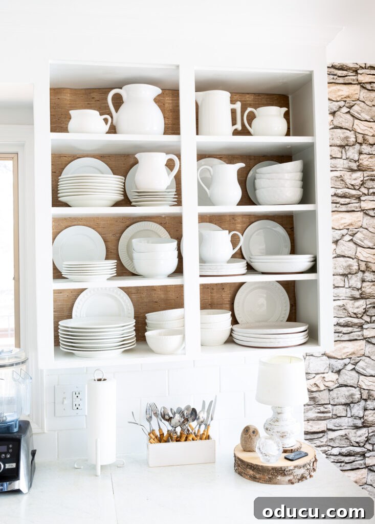 Unveiling Our Open Kitchen Wall 16 The open kitchen shelves, now enhanced with grasscloth wallpaper on their backs, elegantly display a collection of white pitchers, plates, and bowls, creating a serene and cohesive look.