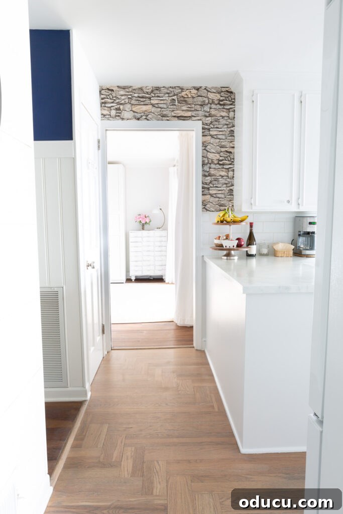 Unveiling Our Open Kitchen Wall 5 A beautifully renovated kitchen space showing the added faux stacked stone wallpaper around the doorway and the freshly painted side of the cabinet, offering a clear view into an adjacent room.
