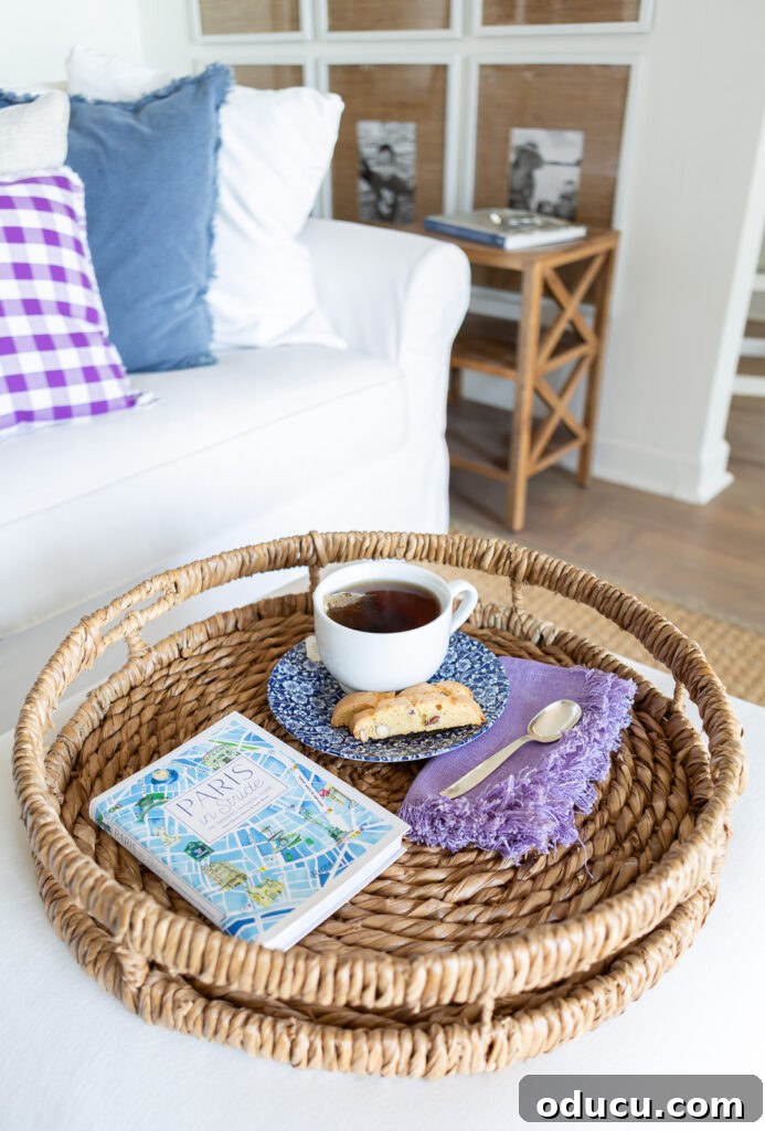 Looking down at a round rattan tray holding a cup of tea, napkin, spoon, a biscotti and a book.