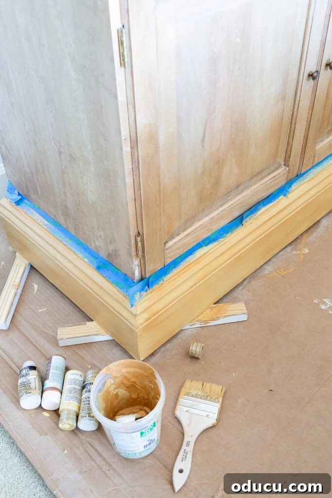 The Transformed Cabinets 7 Applying yellow base coat with a wide chip brush on the bottom trim of a wood cabinet for faux wood grain