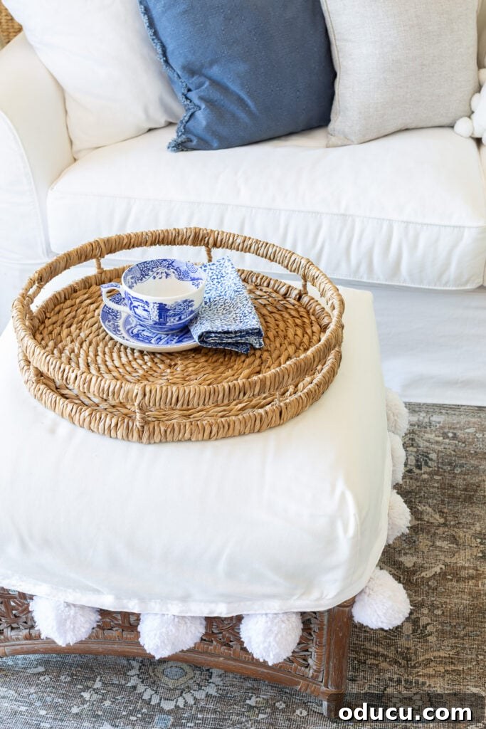A stylish round woven tray gracefully positioned on a white slipcovered ottoman.