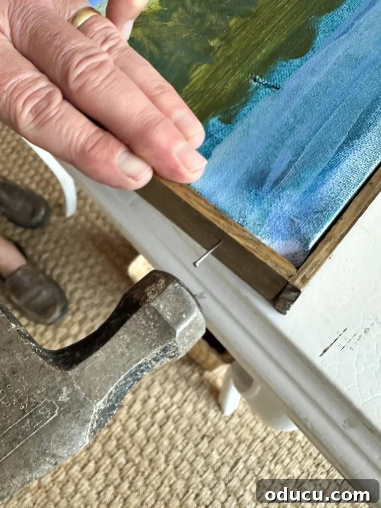 Hammering a nail to attach a wood frame to the custom-painted art canvas.