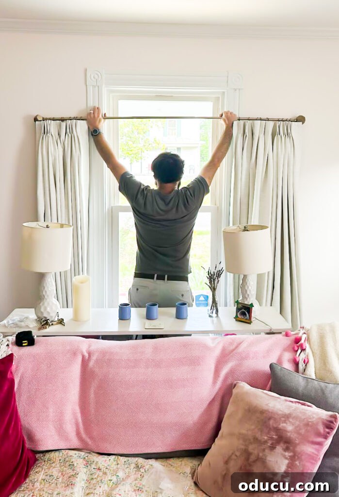 THY Curtains Adorn Every Space Beautifully 9 A man carefully hoisting up a curtain rod with newly attached TwoPages drapes, ensuring perfect alignment and height.