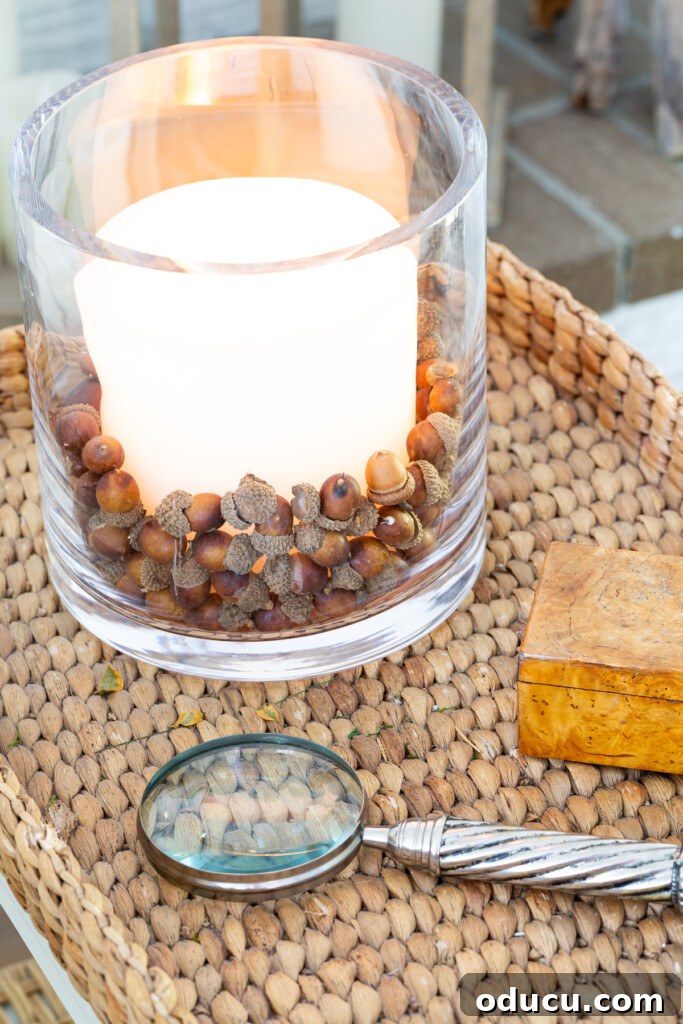 Fall Decor Reimagined 31 faux acorns in glass candle vase on table decorated for fall.