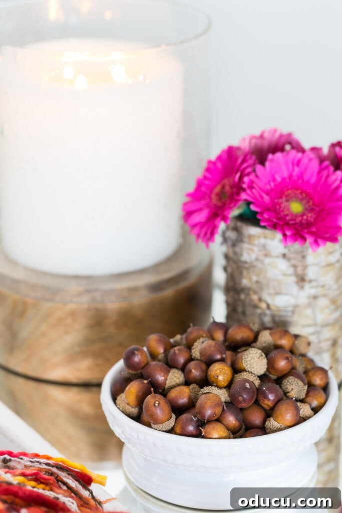 Fall Decor Reimagined 32 a large candle, bowl of acorns and pink flowers on a side table in a living room decorated for fall