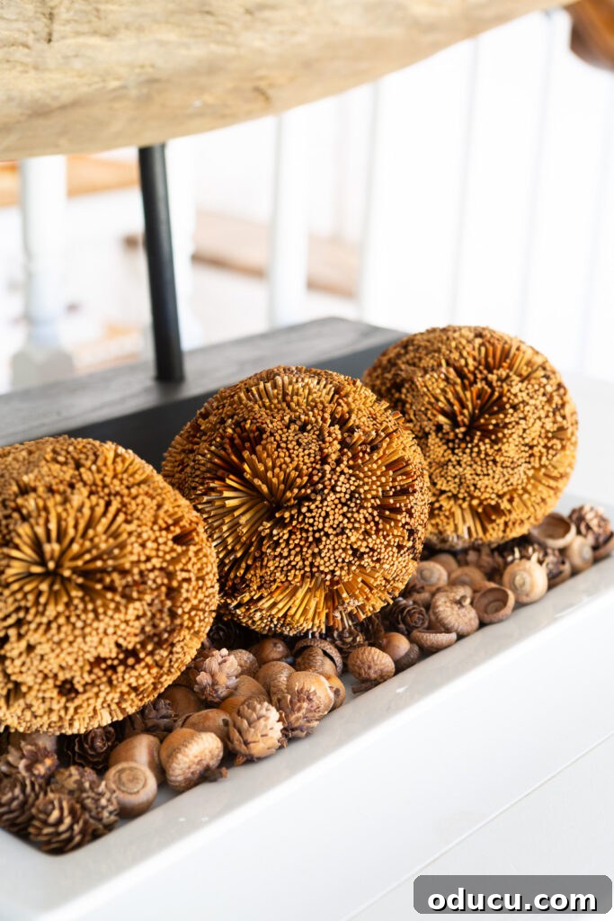 Fall's Full Sensory Home Crafting Your Cozy Autumn Haven 2 Three brown textured spheres resting on a bed of acorns on a white ceramic tray, positioned on a wooden sideboard, creating a simple fall vignette that emphasizes natural elements.
