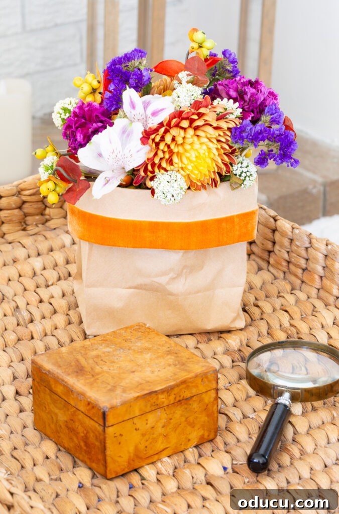 Fall's Full Sensory Home Crafting Your Cozy Autumn Haven 11 A vase of fall flowers elegantly placed in a brown paper bag, secured with an orange velvet ribbon, resting on a side table, offering a rustic yet charming seasonal decoration idea.