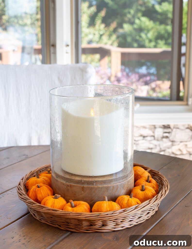 Fall's Full Sensory Home Crafting Your Cozy Autumn Haven 12 A large white pillar candle nestled in a round woven basket tray, surrounded by an arrangement of mini-pumpkins, creating a quintessential cozy fall centerpiece on a table.