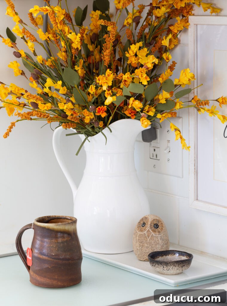 Fall's Full Sensory Home Crafting Your Cozy Autumn Haven 7 A white ceramic pitcher on a kitchen counter filled with vibrant fall foliage, adding a seasonal, natural touch to the culinary space.