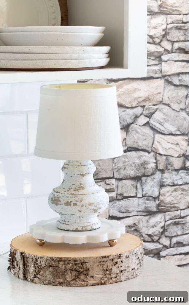 Fall's Full Sensory Home Crafting Your Cozy Autumn Haven 10 An aged white lamp resting on a marble trivet atop a wood tree slice, serving as fall decor on a kitchen counter, enhancing the cozy ambiance with warm light.