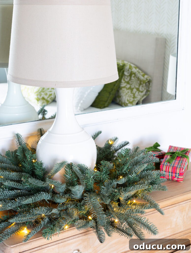 One King of Christmas Fir Set for Three Stunning Holiday Rooms 4 Table lamp on sideboard with a lit Christmas wreath around the base.