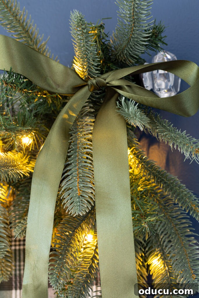 One King of Christmas Fir Set for Three Stunning Holiday Rooms 7 Green satin bow tied onto a King of Christmas Noble Fir garland that is draped on the top of a bed headboard to decorate a bedroom for Christmas.
