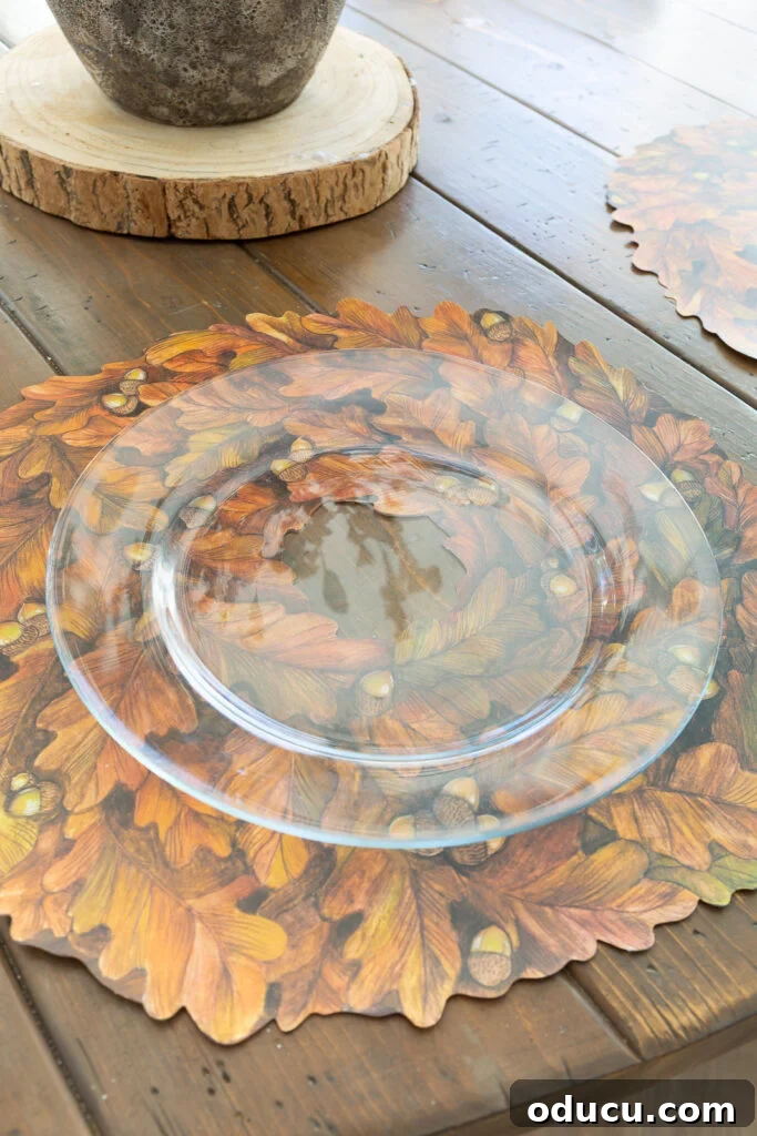 Thanksgiving's Functional and Festive Focal Point 6 A clear glass dinner plate resting on a Hester & Cook 'Autumn Wreath' paper placemat, highlighting the detailed design beneath.