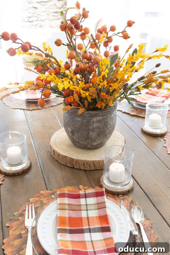 Thanksgiving's Functional and Festive Focal Point 9 A Thanksgiving table centerpiece, a faux fall floral arrangement, elegantly positioned on the center of a round wood dining table set for dinner.