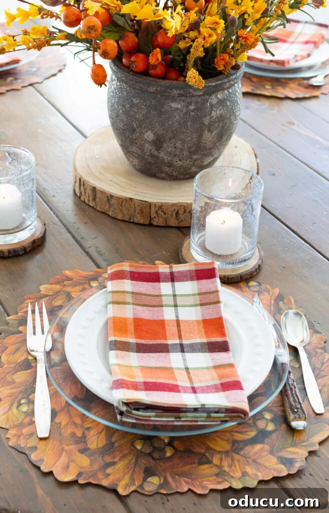 Thanksgiving's Functional and Festive Focal Point 10 A close-up of a Thanksgiving table setting featuring a Hester & Cook fall leaves paper placemat, a plaid napkin, and a clear glass plate.