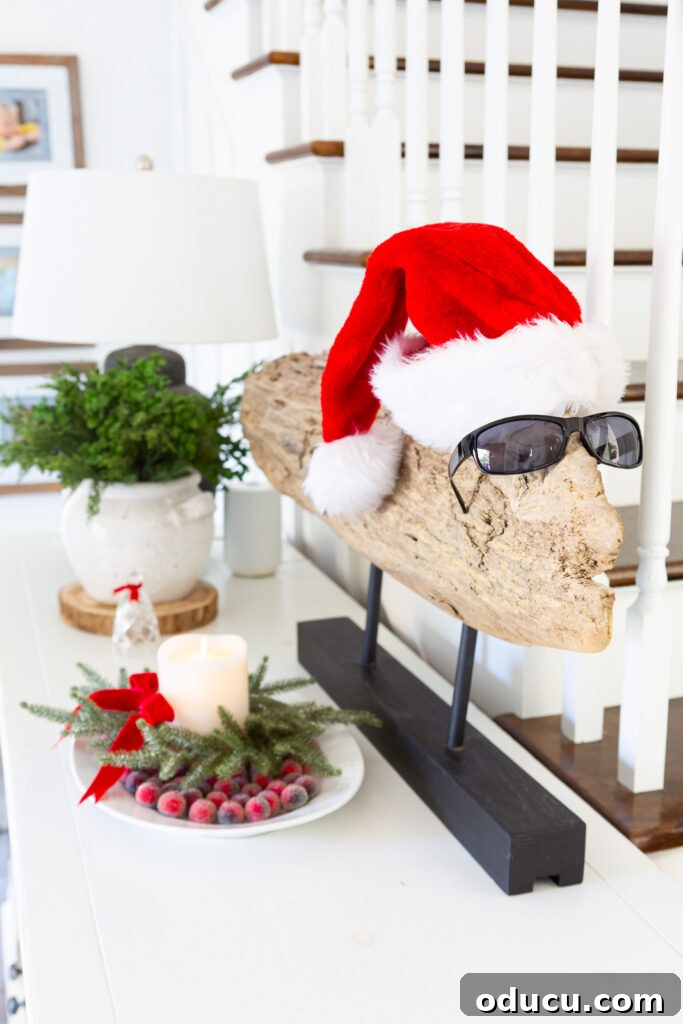 The Wreath Revelation You Need This Christmas 11 A large piece of decorative driftwood, styled as modern art, is playfully topped with a Santa hat and sunglasses, making a quirky Christmas statement on a foyer sideboard.