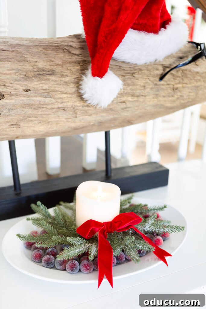 The Wreath Revelation You Need This Christmas 12 A white oval platter is elegantly arranged with sugared cranberries, a small wreath, a white candle, and a red velvet bow, creating a beautiful Christmas centerpiece.